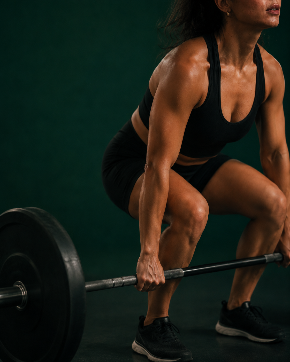 Coach lifting a barbell in a dark green studio.