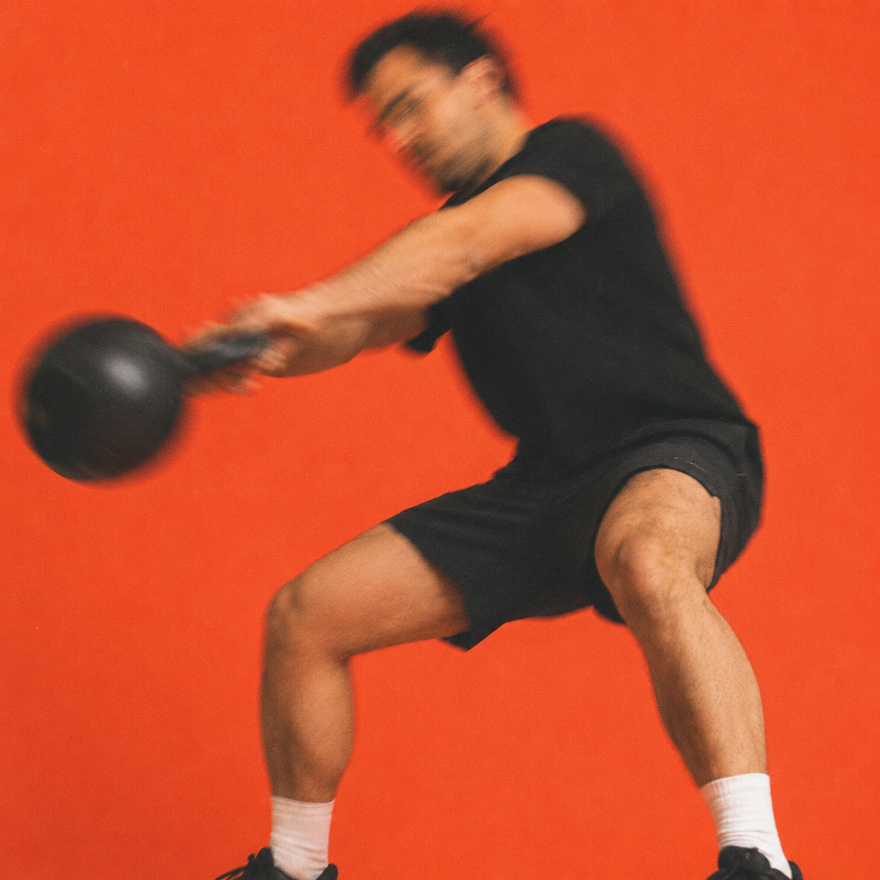 Person training dynamically with a kettlebell against an orange backdrop.